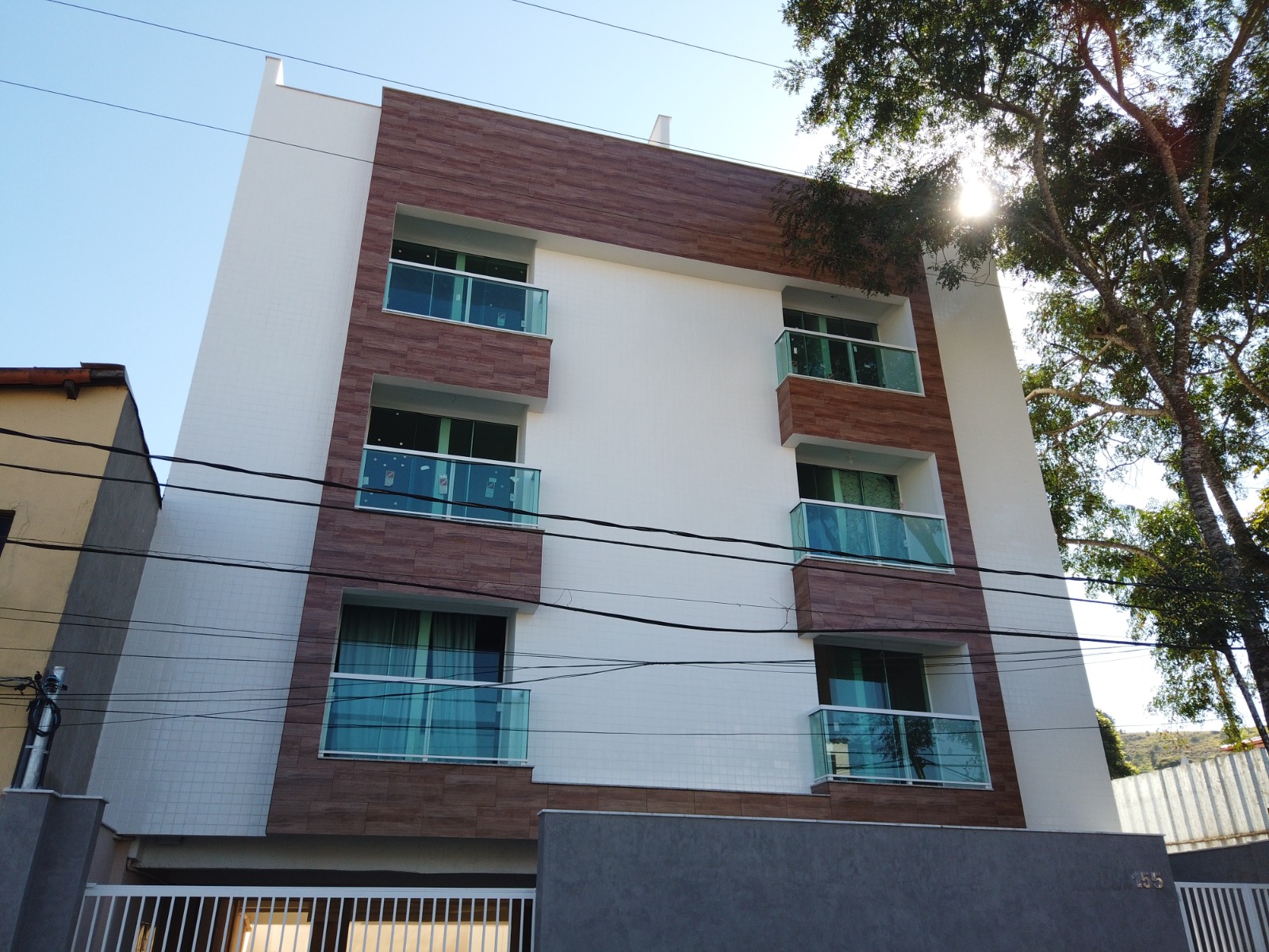 Fachada de edifício residencial de quatro pavimentos com varandas em vidro e revestimento amadeirado