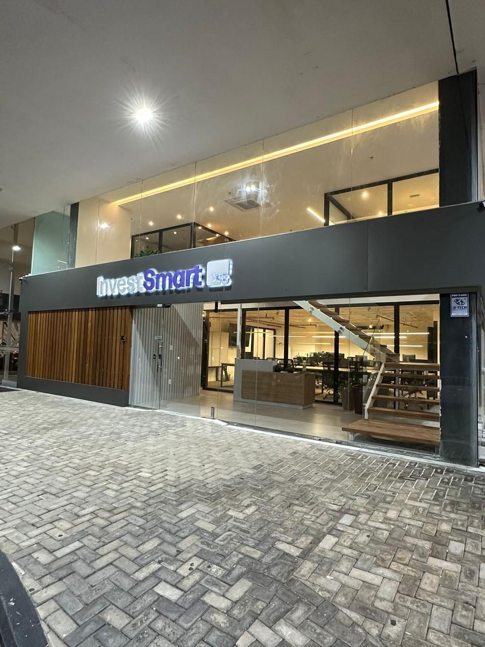 Fachada de escritório corporativo em vidro, com marquise escura e iluminação interna acesa