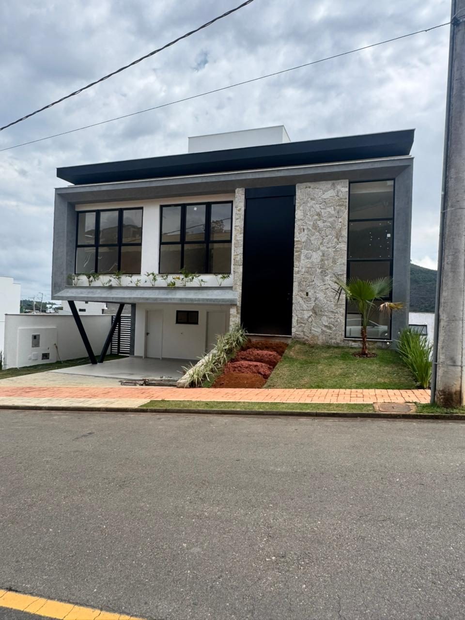 Residência de dois pavimentos com base em pedra, volumes brancos e garagem coberta