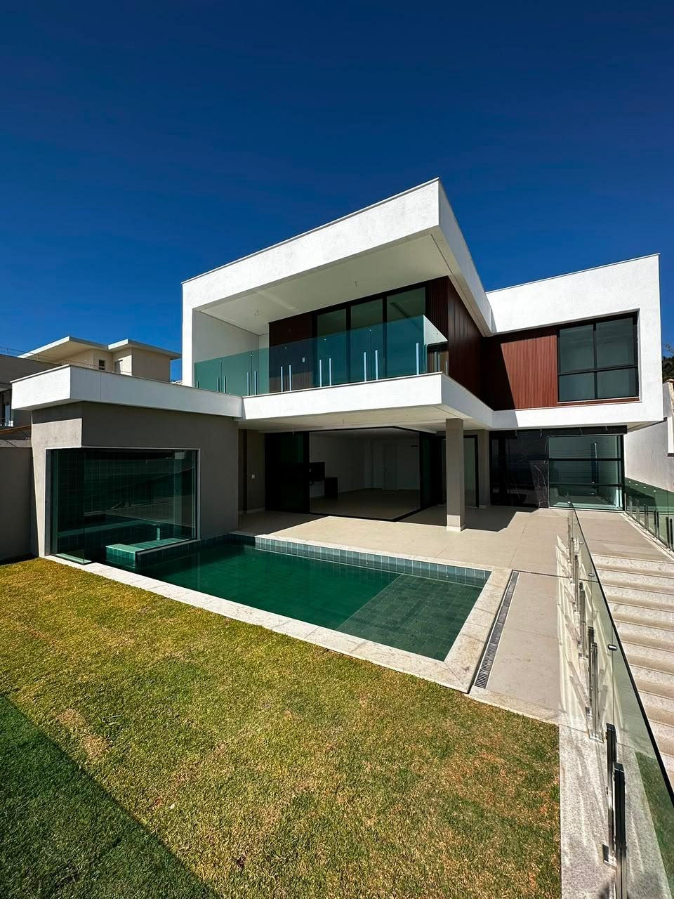 Residência de dois pavimentos com volumes brancos, esquadrias escuras e piscina no jardim lateral