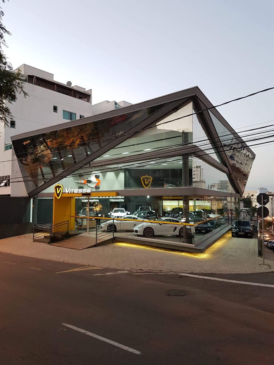 Loja comercial em esquina com fachada em vidro, estrutura metálica inclinada e iluminação noturna