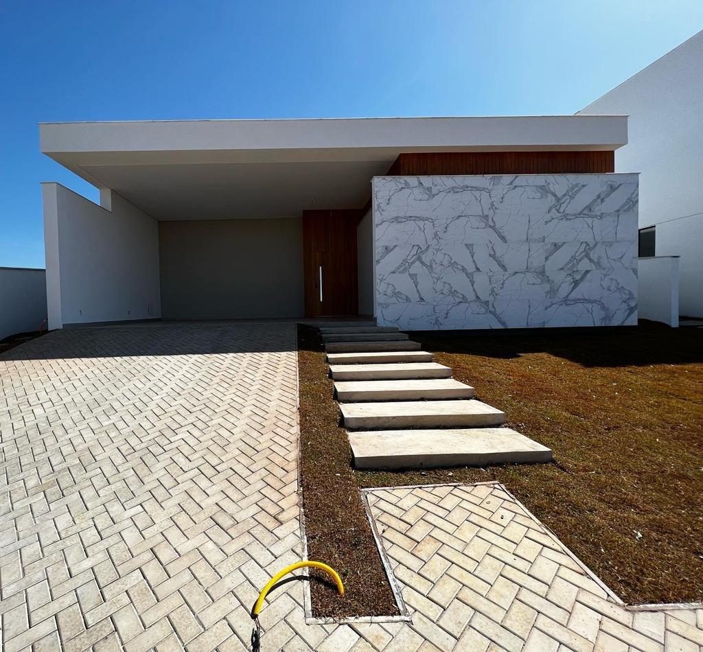 Fachada de residência branca com grande painel de mármore e caminho de placas de pedra sobre o jardim